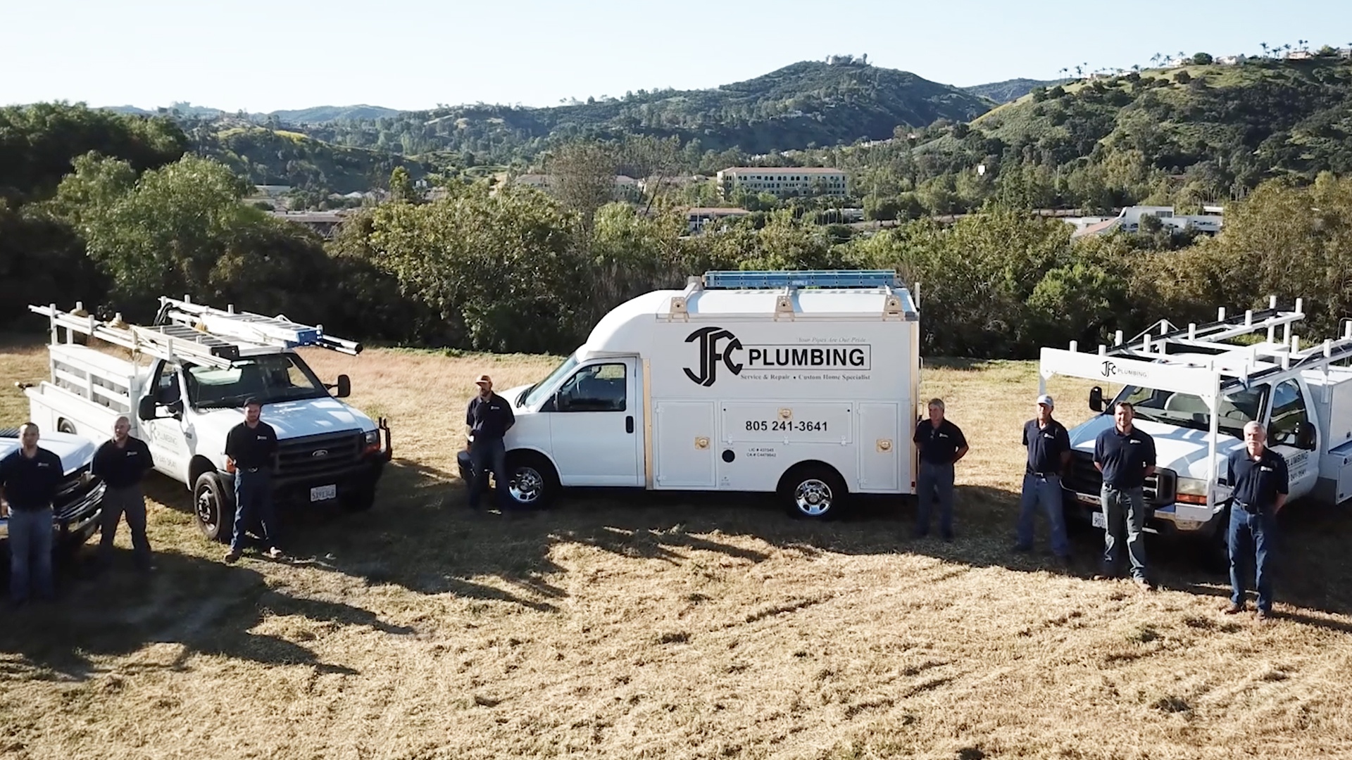 JFC Plumbing vehicles and employees in front of a scenic landscape and mountain