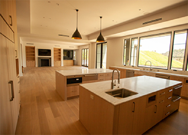 View of a kitchen with two islands and an empty living space with built-in bookshelves, a fireplace, and a TV