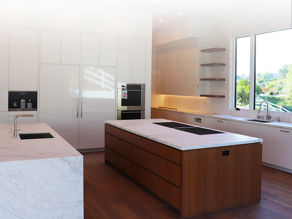 A remodeled kitchen with white marble countertops, a dark wood island, and glossy white cabinets in the rest of the kitchen