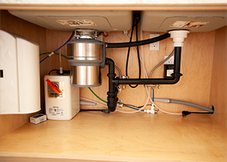 A garbage disposal and piping beneath a sink inside a cabinet