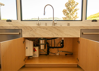 Open cabinet doors showing a garbage disposal and piping beneath a kitchen sink