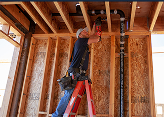 A JFC plumber on a ladder working on piping in the ceiling of a home that is not yet completed